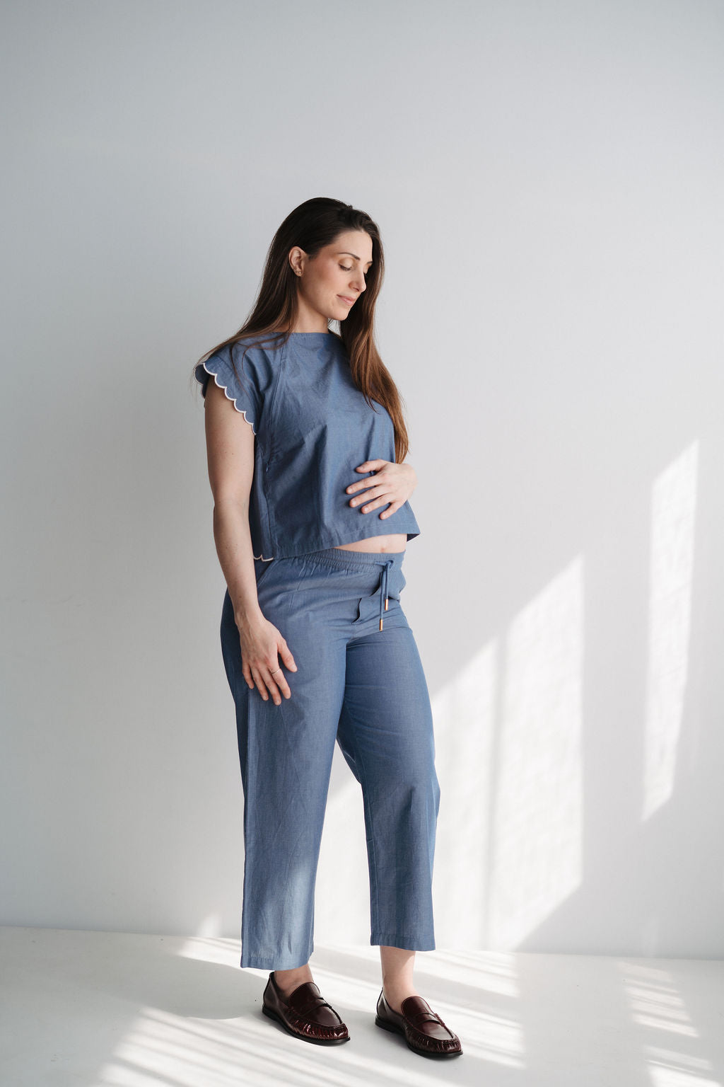 Femme enceinte en pantalon bleu et haut coordonné dans un intérieur lumineux