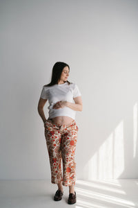 Femme enceinte souriante portant un pantalon de maternité imprimé aux motifs indiens rouges et verts