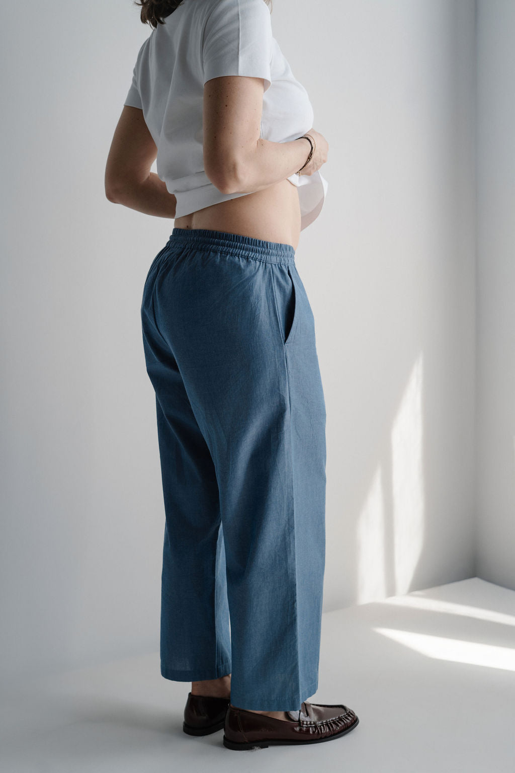 Femme enceinte en pantalon de maternité bleu souriant face à l'objectif